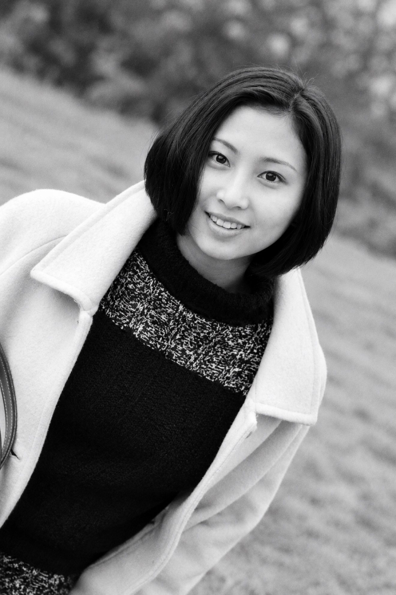 黑白照片：身穿白色大衣的短发女子在户外微笑望向镜头