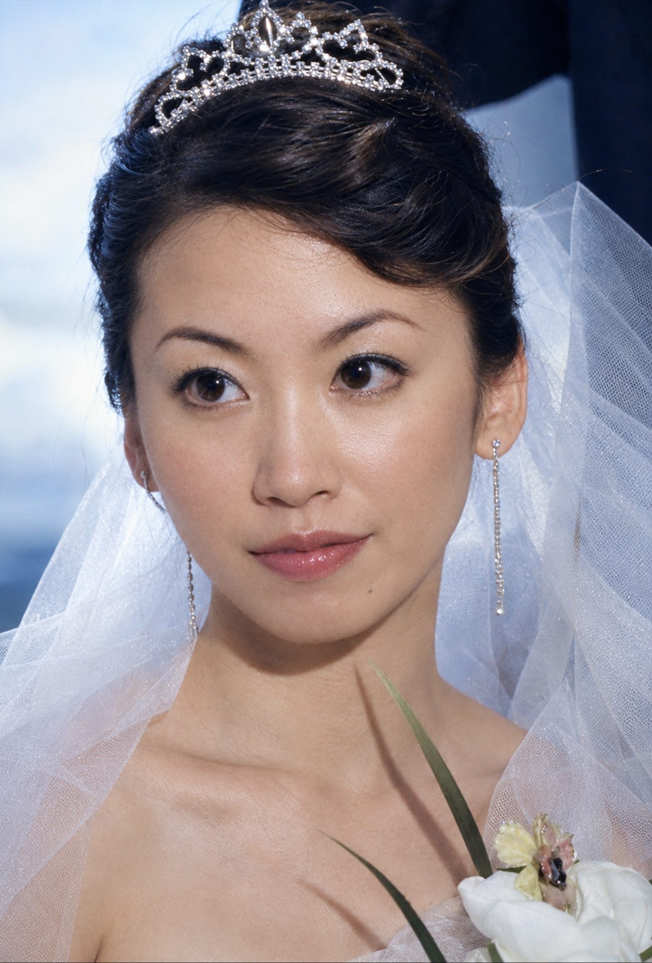 彩色照片：头戴皇冠与头纱、身穿婚纱的女子面部特写，望向镜头，右下角露出一束捧花