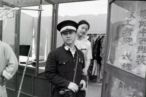 黑白照片：吴江大上海餐饮活动，穿制服戴大檐帽的男子站在前景，身后穿旗袍的女子探身望向镜头，右侧玻璃上写着中西服装字样